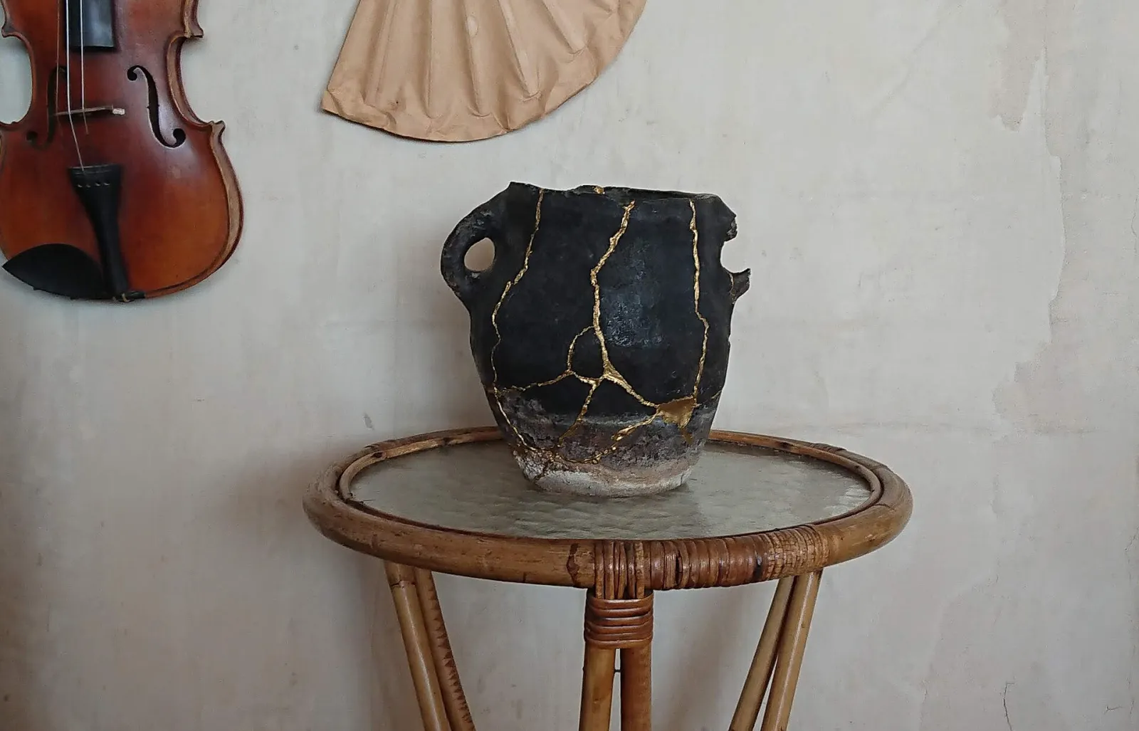 A black clay jar on a rattan table, its many cracks joined with bright gold seams.